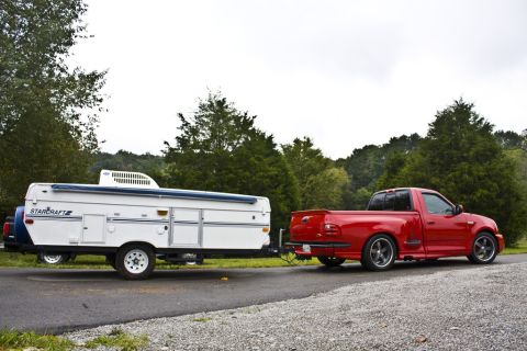 2007 Ford Mustang - A red Ford F-150 Lightning pickup truck tows a Starcraft pop-up camper on a paved road with trees in the background.