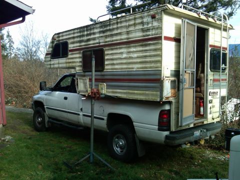 1978 Ford Bronco - A white pickup truck is fitted with a camper shell, parked outdoors on a grassy area.