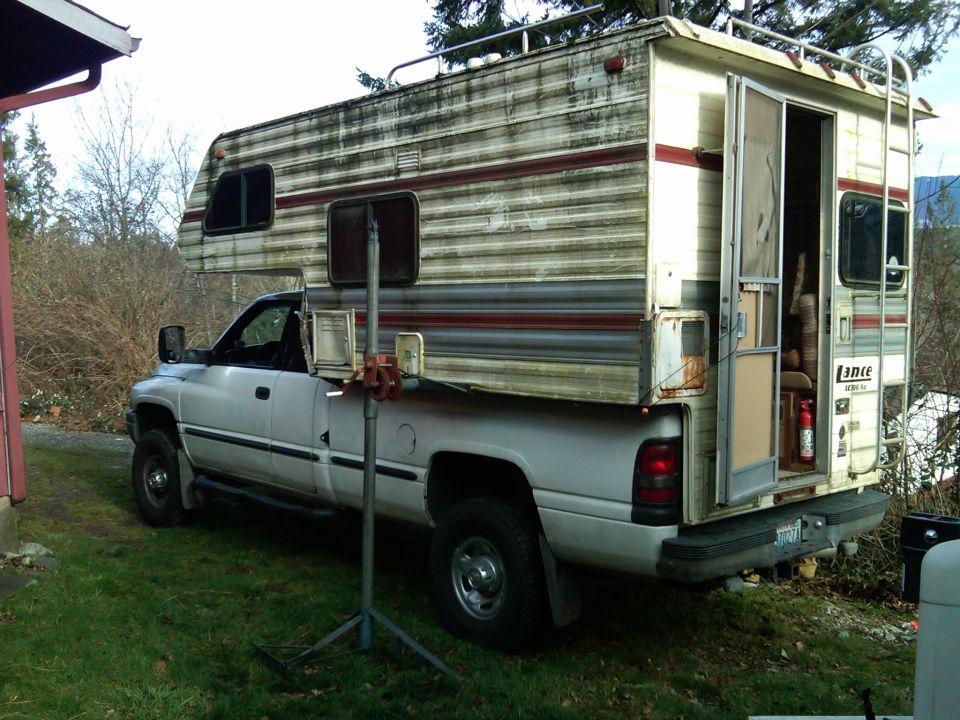 White pickup truck with a cream and red striped camper shell, viewed from the side