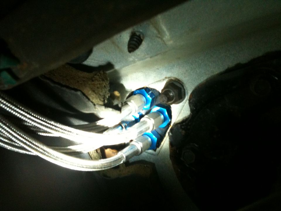 Braided stainless brake lines with blue anodized fittings mounted on a white frame bracket