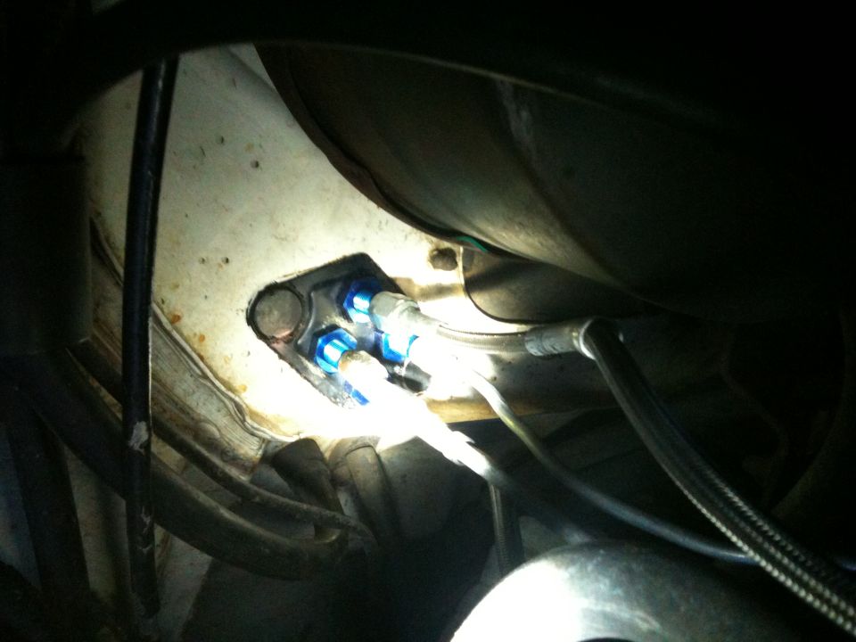 Blue anodized AN fittings and braided lines mounted under a vehicle, lit by flash