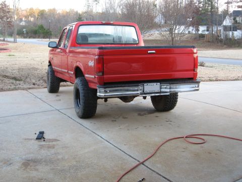 1995 Ford F-150 - The rear view of a red 1995 Ford F-150 pickup truck with a lifted suspension and large tires.