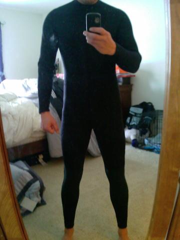 1995 Ford Probe - A person in a black wetsuit takes a mirror selfie in a bedroom, holding a cell phone.