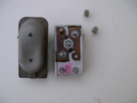 1998 Ford Crown Victoria - A disassembled car window switch and its electrical components are laid out on a white surface.