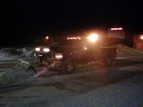 2006 Ford F-350 - A truck equipped with a snow plow operates in snowy conditions during the night.