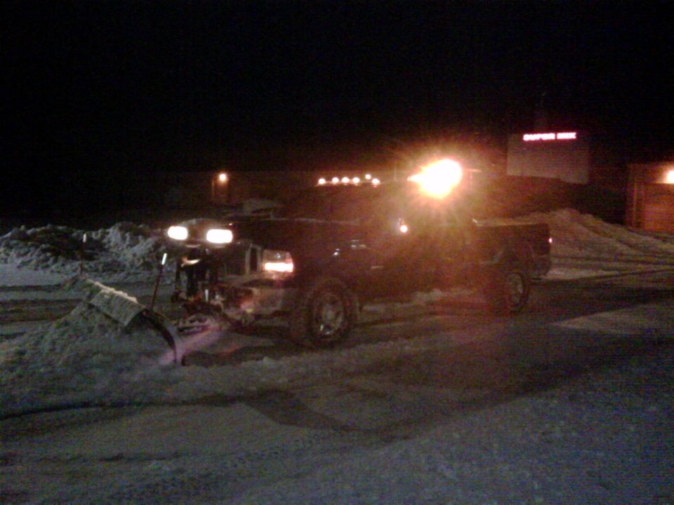 Truck with a snow plow attached, clearing snow at night