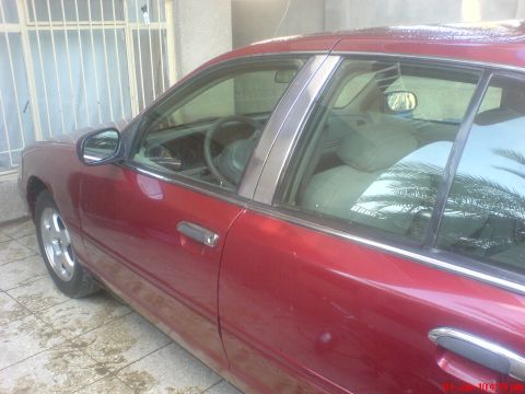 1998 Ford Crown Victoria - Side view of a red 1998 Ford Crown Victoria sedan parked outdoors.