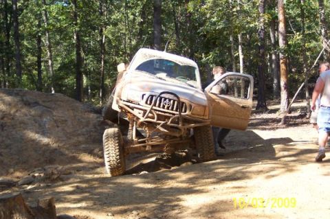 1996 Ford Bronco - A mud-splattered off-road truck is shown on a dirt trail with its driver's side door open.