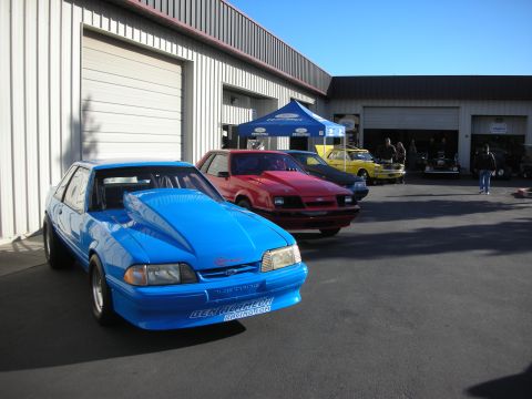 1992 Ford Crown Victoria - Several cars are parked outside a building with garage doors, under a blue tent.