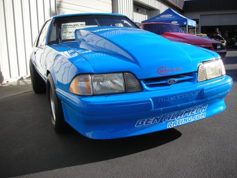 1992 Ford Crown Victoria - A bright blue Ford Mustang with a prominent hood scoop and racing decals is parked outside a building.