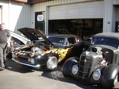 1992 Ford Crown Victoria - Custom hot rods with flame graphics and exposed engines parked outside a garage.
