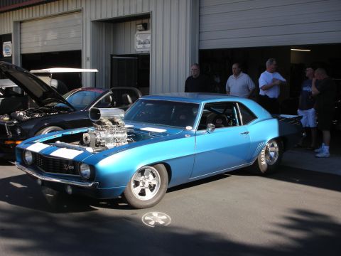 1992 Ford Crown Victoria - A bright blue 1969 Camaro with a prominent supercharger is displayed outside a garage, with other vehicles and people nearby.