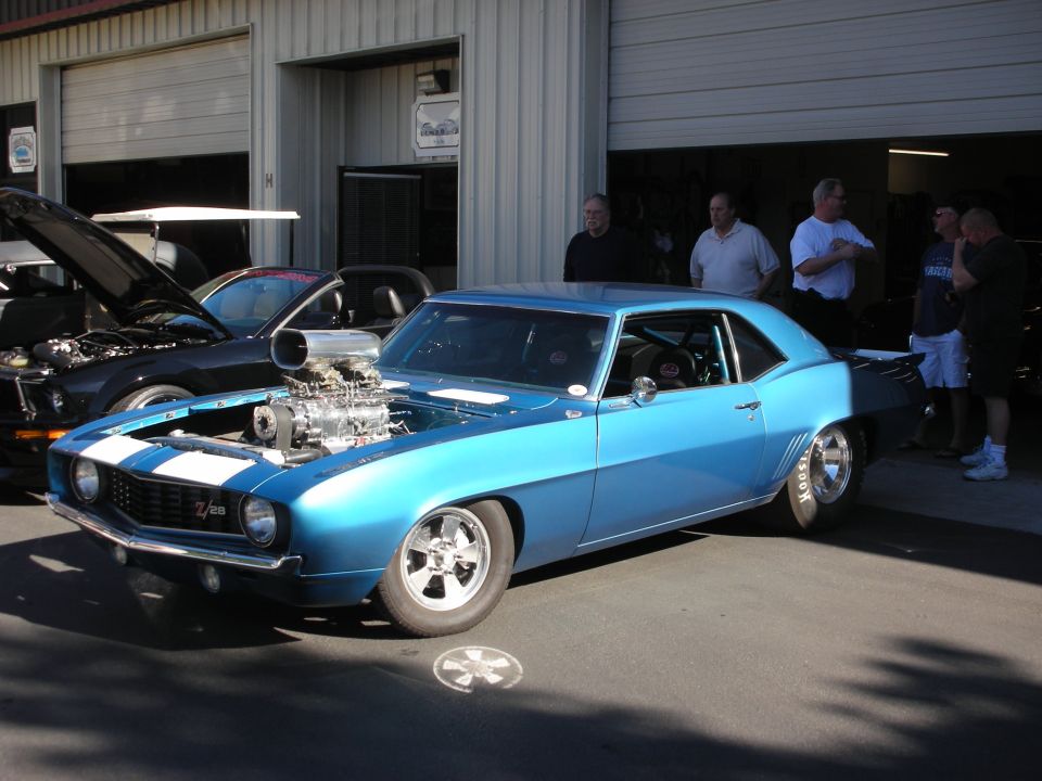 Blue 1969 Camaro with a big supercharger sticking out of the hood, parked next to a black car with its hood up