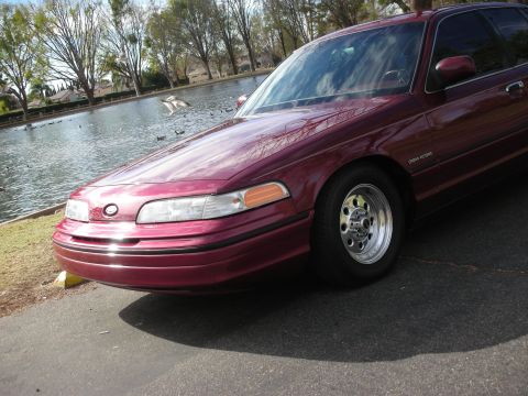 1992 Ford Crown Victoria - A maroon 1992 Ford Crown Victoria is parked next to a lake with several ducks swimming.