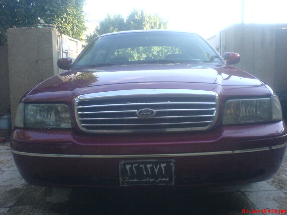 Front view of a maroon Ford Crown Victoria with a chrome grille and a license plate with Arabic text