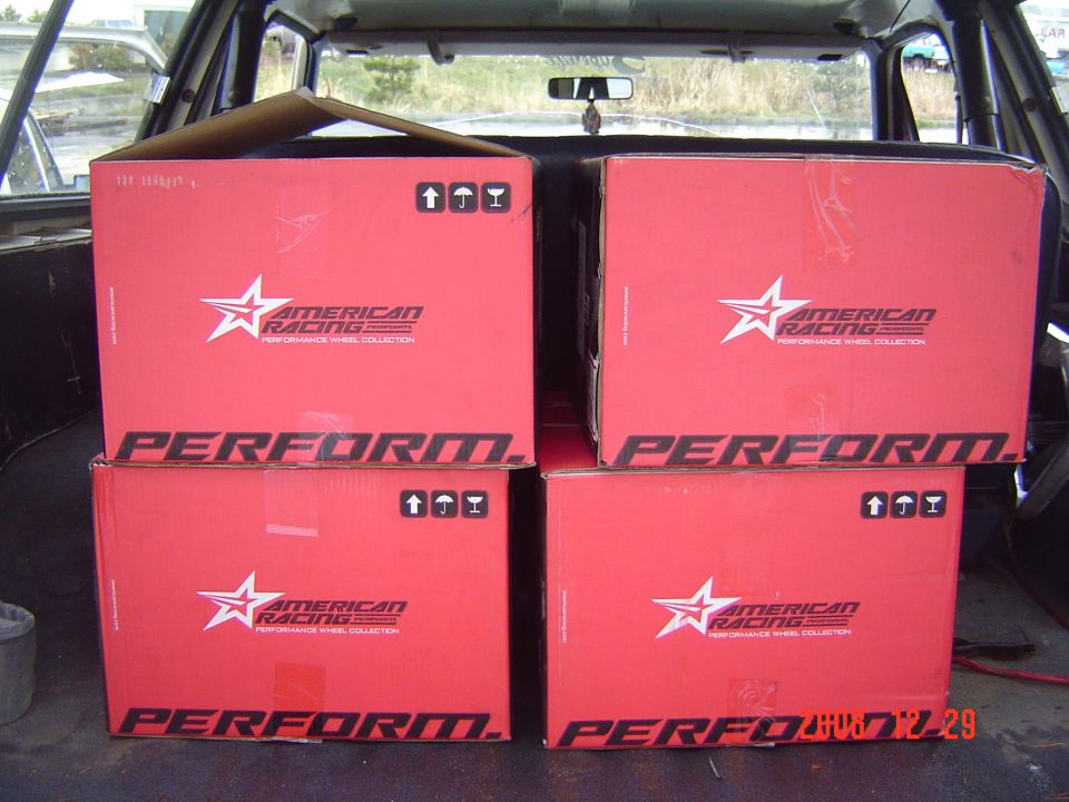 Four red American Racing wheel boxes stacked in the cargo area of a vehicle