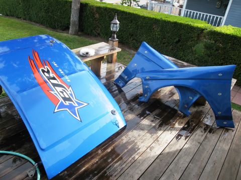 1986 Ford Bronco - Blue hood and fender set with racing decals, photographed on a wooden deck.