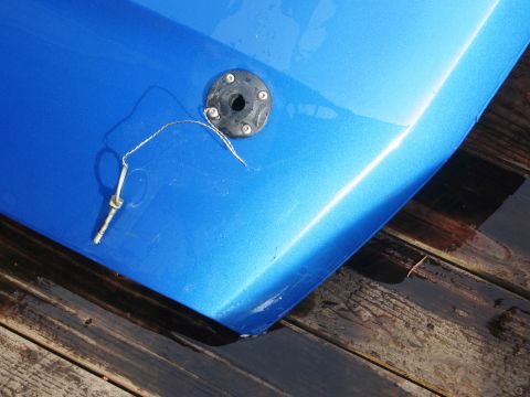 1986 Ford Bronco - Close-up of a blue car hood showing a fuel cap and tether pin.