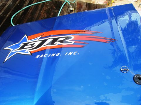1986 Ford Bronco - A blue hood with racing decals is shown, with a hood pin visible on the surface.