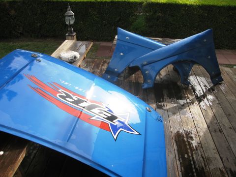 1986 Ford Bronco - Blue hood and fenders with racing decals are laid out on a wooden deck.
