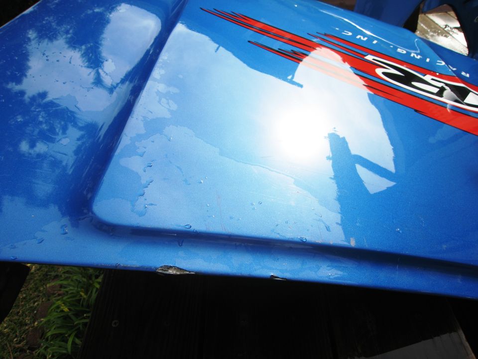 blue car fender with red and black racing stripes and "RACING INC." text. Some water droplets on surface
