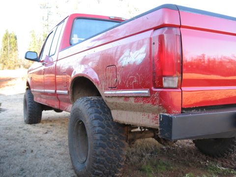 1995 Ford F-150 - Rear view of a red 1995 Ford F-150 pickup truck, showing mud on the body and a custom bumper.