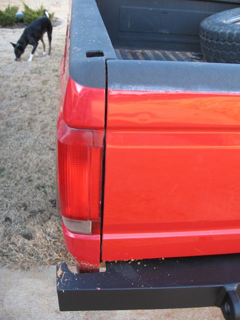 1995 Ford F-150 - The rear corner of a red pickup truck is shown, with a black bumper and a spare tire visible in the bed.