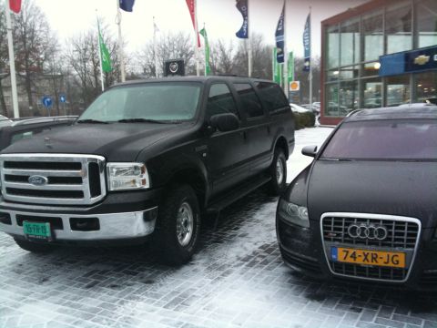 2005 Ford Excursion - A black Ford Excursion is parked on a snowy lot next to a dark Audi sedan.