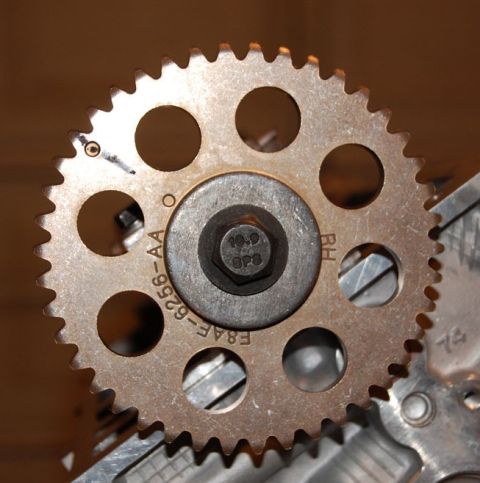 2007 Ford Mustang - A close-up view of a metal engine timing gear, showing stamped part numbers and a central bolt.