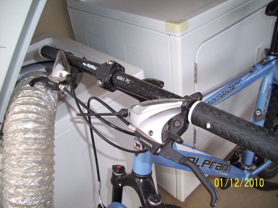 Blue bicycle handlebars with Shimano shifters and "Tomahawk" frame visible next to a dryer