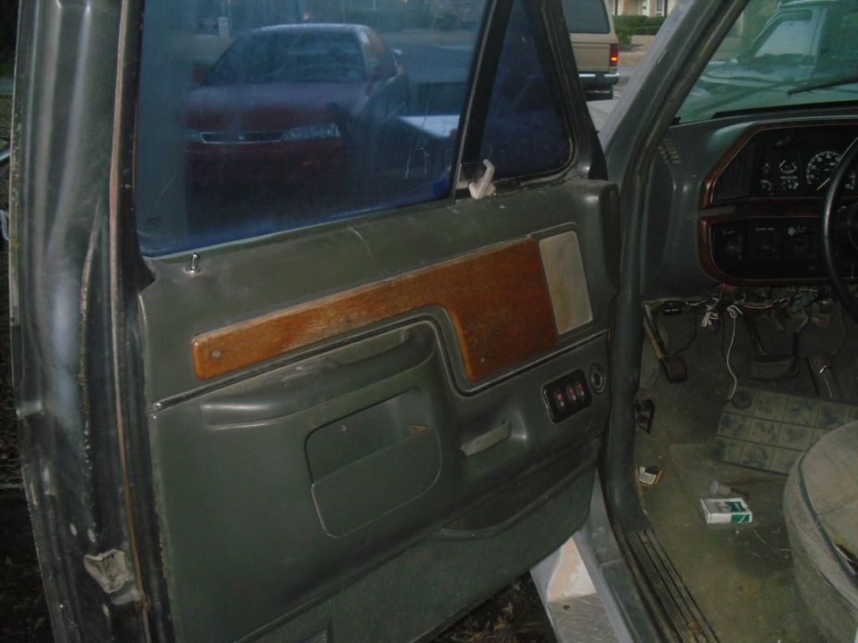 Gray interior of a Ford truck, showing the driver's side door panel with wood trim and the dashboard with gauges. A cigarette pack is on the floor
