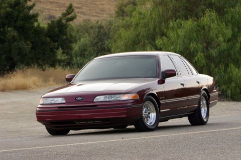 1992 Ford Crown Victoria - Three-quarter front view of a dark maroon Ford full-size sedan with an aero nose, body-color grille bar and Ford blue oval, sitting low on…