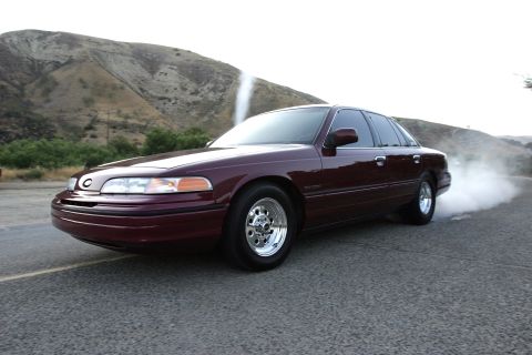 1992 Ford Crown Victoria - A burgundy early-1990s Ford Crown Victoria performs a burnout on a two-lane road, tire smoke billowing behind the rear wheels as it rides o…