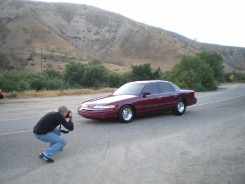 1992 Ford Crown Victoria - Burgundy Ford Crown Victoria sedan with polished aftermarket wheels parked on a roadside pullout below dry brush-covered hills, while a cro…