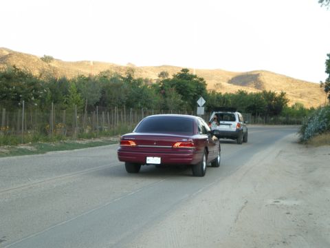 1992 Ford Crown Victoria - Dark red Ford Crown Victoria sedan photographed from directly behind on a two-lane rural road, brake lights lit, showing the full-width tai…