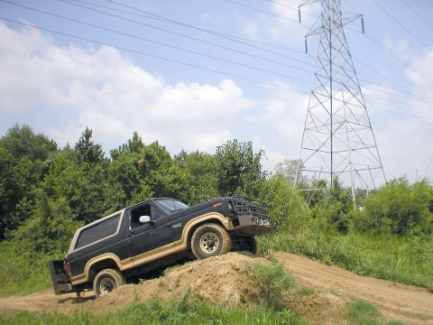 1983 Ford Bronco - Ford Bronco navigates an off-road trail with a large power line tower in the background.
