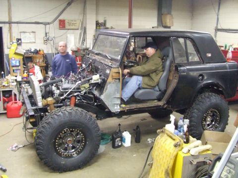 1967 International Scout 800 - A black 1967 International Scout 800 is shown in a workshop with its doors open and engine exposed, undergoing work.