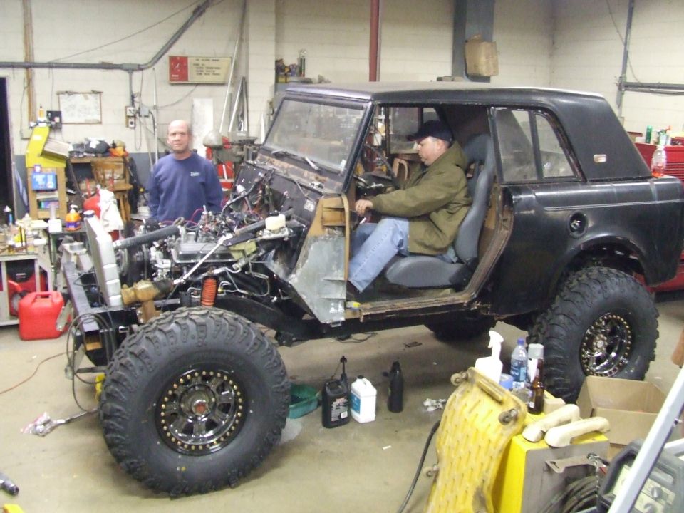 Black Scout SUV under build on big off-road tires in garage, man seated inside