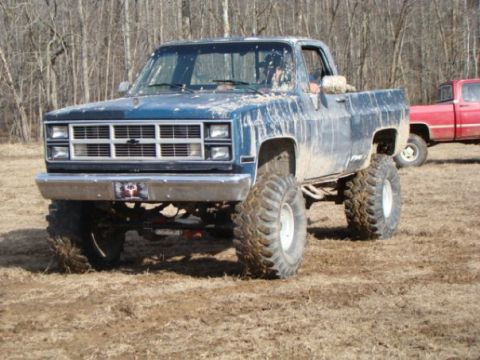 1979 Ford Bronco - A lifted blue pickup truck sits in a muddy field with a red truck visible behind it.