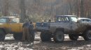 1979 Ford Bronco - Two pickup trucks are stuck in the mud with trees in the background.