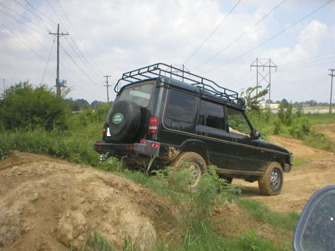 1983 Ford Bronco - A dark green Land Rover Discovery navigates an off-road trail with a roof rack and spare tire visible.