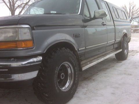 1994 Ford F-150 - This Ford F-150 pickup truck features a two-tone gray paint scheme and a camper shell, viewed from the front quarter.