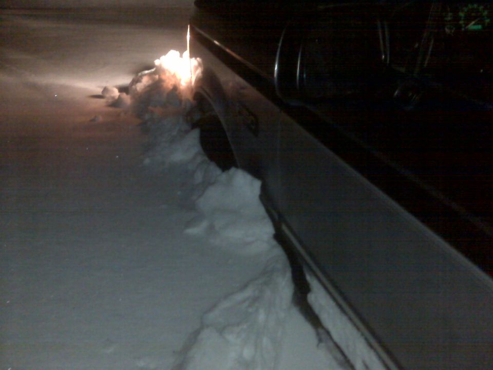 Truck stuck in deep snow, headlights on, pushing snow