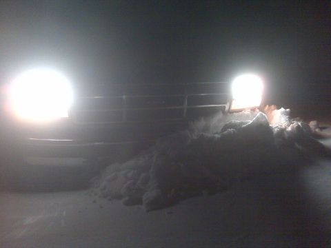 1994 Ford F-150 - A truck's front end is visible at night, partially obscured by snow, with headlights on.