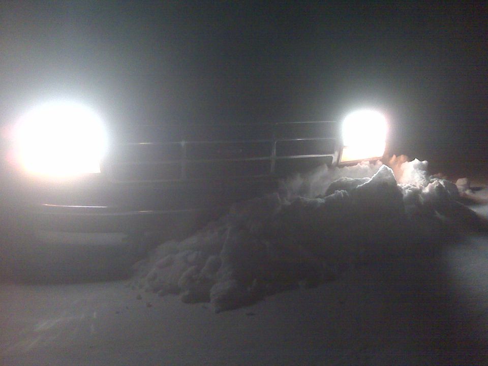 Truck grille and headlights illuminated at night, with snow piled in front
