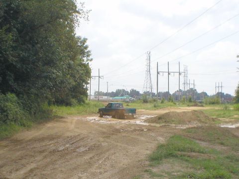 1983 Ford Bronco - A green pickup truck navigates a muddy track, kicking up water and dirt.