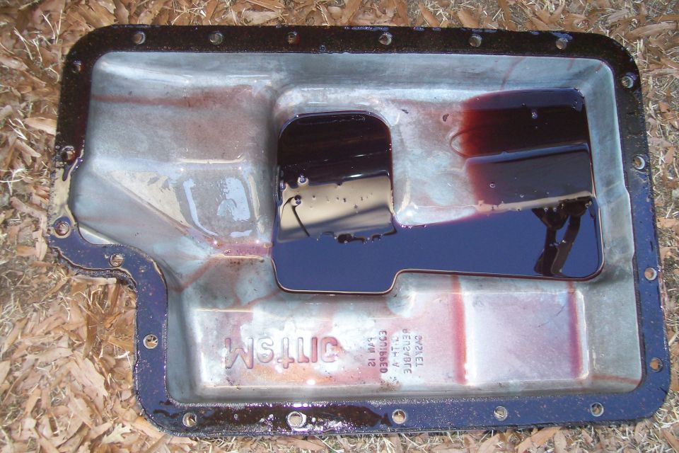 Transmission pan with dark fluid and some residue. Text is visible on the pan