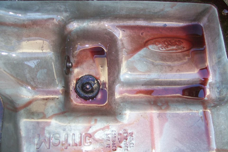 Transmission pan with dark red fluid and a Ford logo embossed in it. There's a drain plug visible