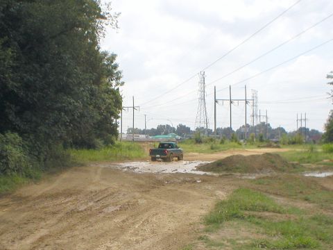 1983 Ford Bronco - Truck navigates a muddy obstacle course under a cloudy sky with power line towers visible.