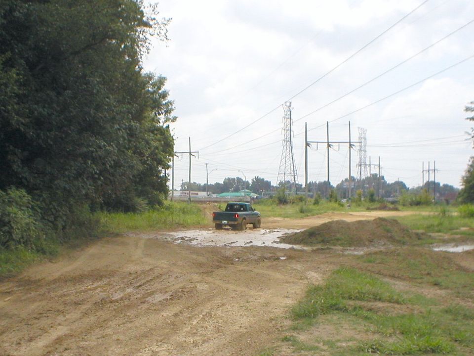 Rear view of dark pickup truck driving through mud on a dirt track near power lines